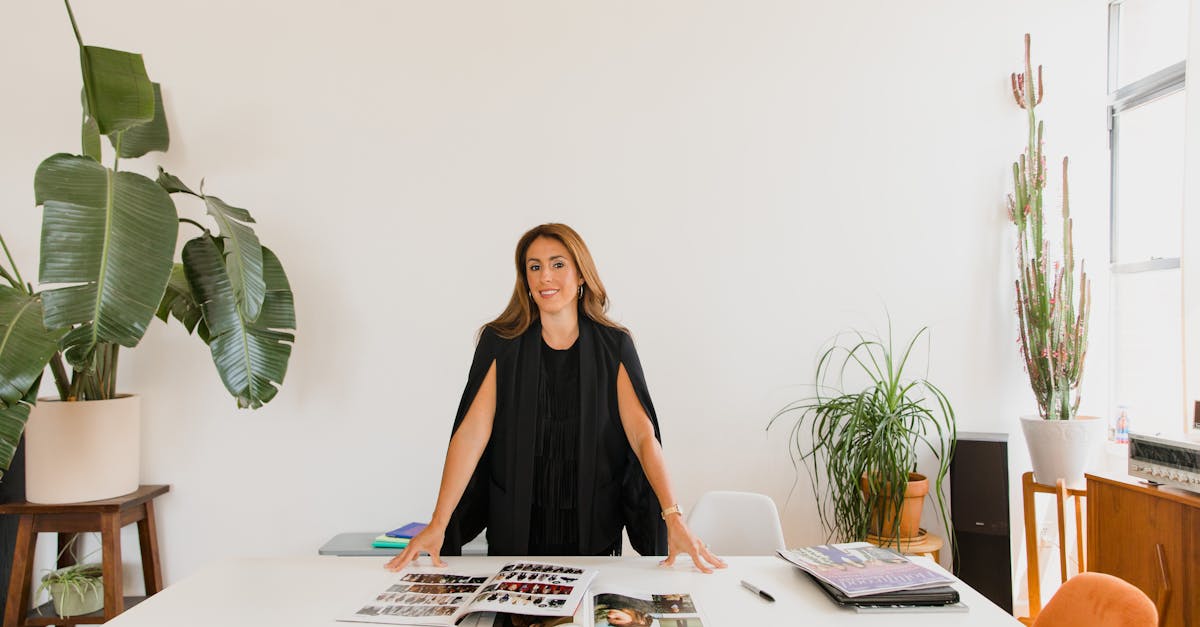 Elegant businesswoman standing confidently at a desk with magazines and indoor plants.